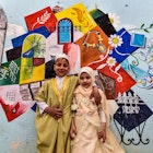 Children pose for a photo in front of a large graffiti depicting cultural elements including mosques, churches, old window lattices of the old town of Iraq's northern city of Mosul, on the first night of the Muslim holy fasting month of Ramadan on April 13, 2021, during a celebration hosted by a local cultural NGO. (Photo by Zaid AL-OBEIDI / AFP) (Photo by ZAID AL-OBEIDI/AFP via Getty Images)